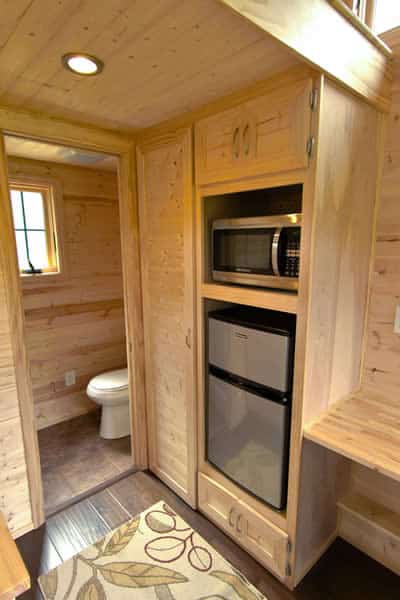 小厨房设有紧凑型冰箱和微波炉内置架子，浴室在背景。