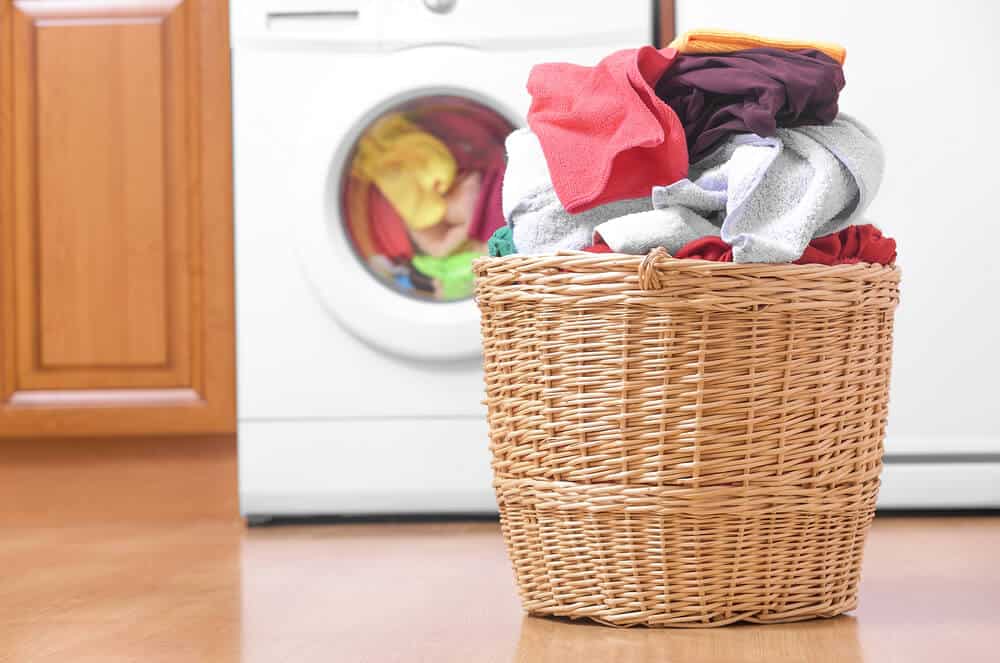 将装满衣服的洗衣篮放在洗衣机前洗衣。