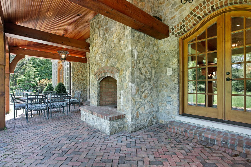 这个壁炉建在住宅石头立面的一侧，完美融合。它延伸到露台的木质屋顶顶部，并有一个凸起的壁炉，与露台的砖块相匹配。