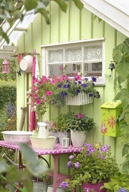 一个可爱的春天绿色花园小屋，装饰着许多鲜花和园艺配件的容器。一个粉红色的小桌子靠在外墙，一个伟大的工作站!