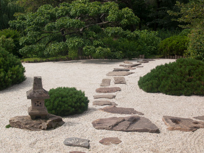 这个禅宗花园的重点是沙子和石头，但有几片坚固，浓密的灌木。