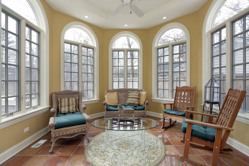一间铺着瓷砖的阳光房，有装饰性的地毯，传统的椅子和一张玻璃桌。