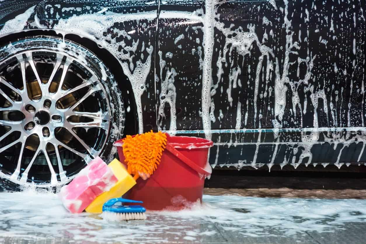不同类型的洗车工具和一辆湿肥皂黑色汽车后面。