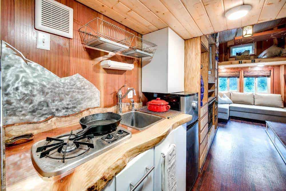 一个微型家庭厨房的特写照片，自定义木制品，水槽，橱柜，后挡板和范围。