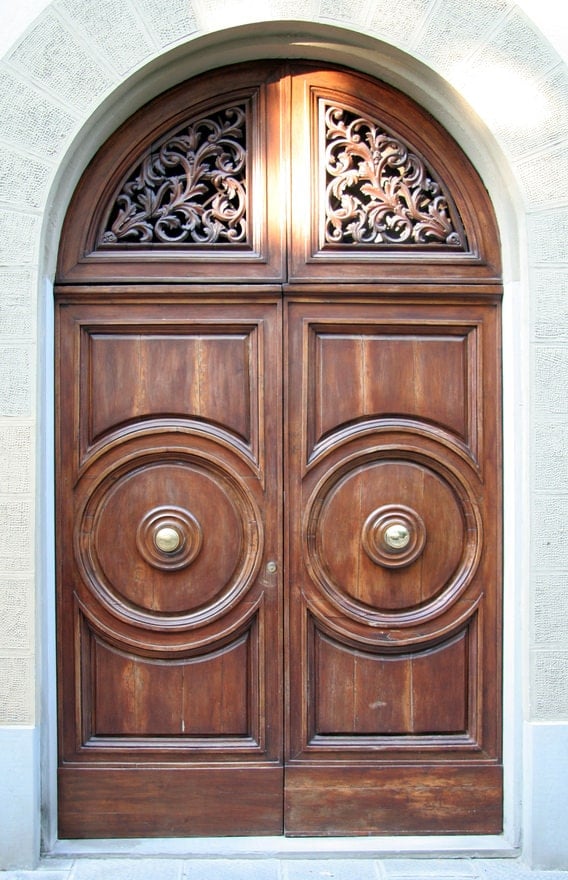 另一扇经典的拱形木门，带有复杂的雕刻和装饰。一对黄铜旋钮完成了整个造型。