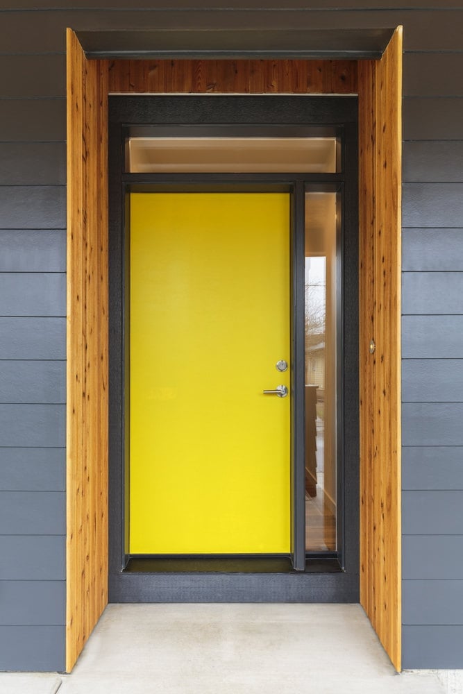 一扇黄色的前门，带有侧玻璃板和横梁窗。尽管它的设计简单，但它充满活力的颜色使它在灰色的墙壁上脱颖而出。
