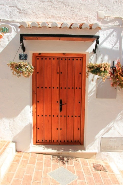 希腊房子上的木板门，上面有铁的细节，屋顶下固定着可爱的悬挂植物。