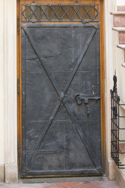 一个质朴的金属前门展示了一个x型装饰和一个横梁窗对着木制背景。