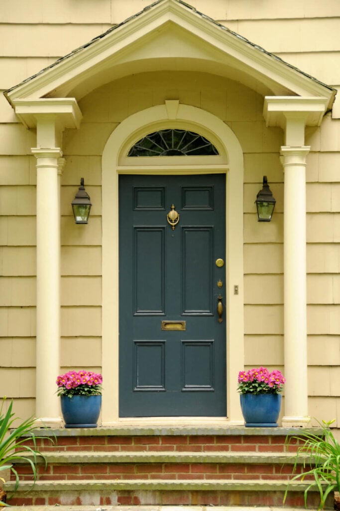 白色的柱子和一对壁式烛台，以及可爱的盆栽植物，与装有黄铜五金的蓝色前门完美对称。