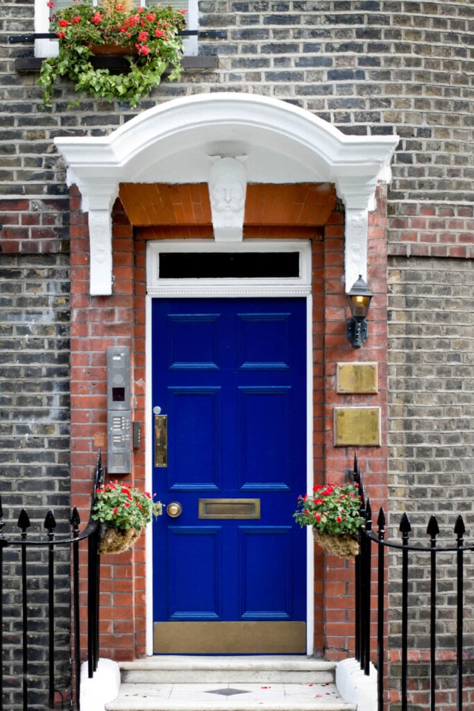 这栋房子里有一扇充满活力的蓝色门，砖墙和头部雕塑设计的门廊格外显眼。它由安装在黄铜板上方的壁灯照明。