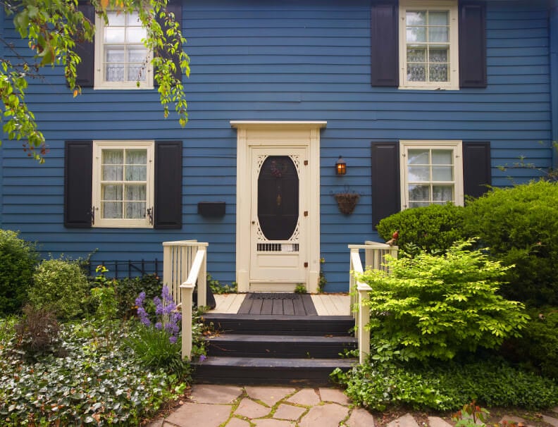铺着石板的铺路石和一段镶着白色栏杆的深色木楼梯，通往这扇迷人的前门，大门上有一盏琥珀色的壁灯。加上装有深蓝色百叶窗的白色框窗，它们都为这座蓝色的房子增添了个性。