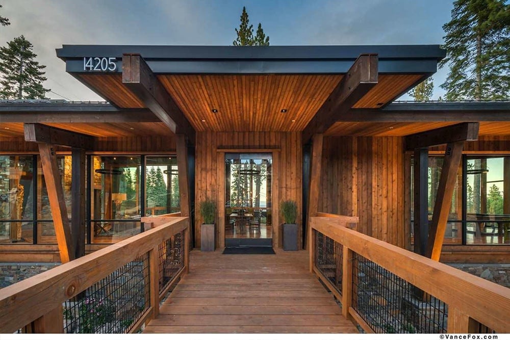 玻璃前门为这座全木住宅增添了现代气息，金属栏杆框架的木栈桥。它是由光滑的花盆和黑色小地毯补充。