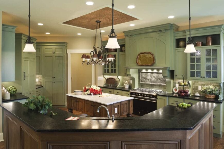 这是一个可爱的厨房，其中绿色橱柜的使用有利于厨房的整体美感。它提供了一种赏心悦目的美学，特别是棕色厨房岛岛和硬木地板以及棕色天花板和棕色吊灯的补充。