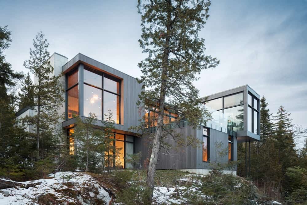 现代住宅拥有时尚的外观，玻璃门窗。周围的环境提供了健康的绿色植物，而大地被白雪覆盖。