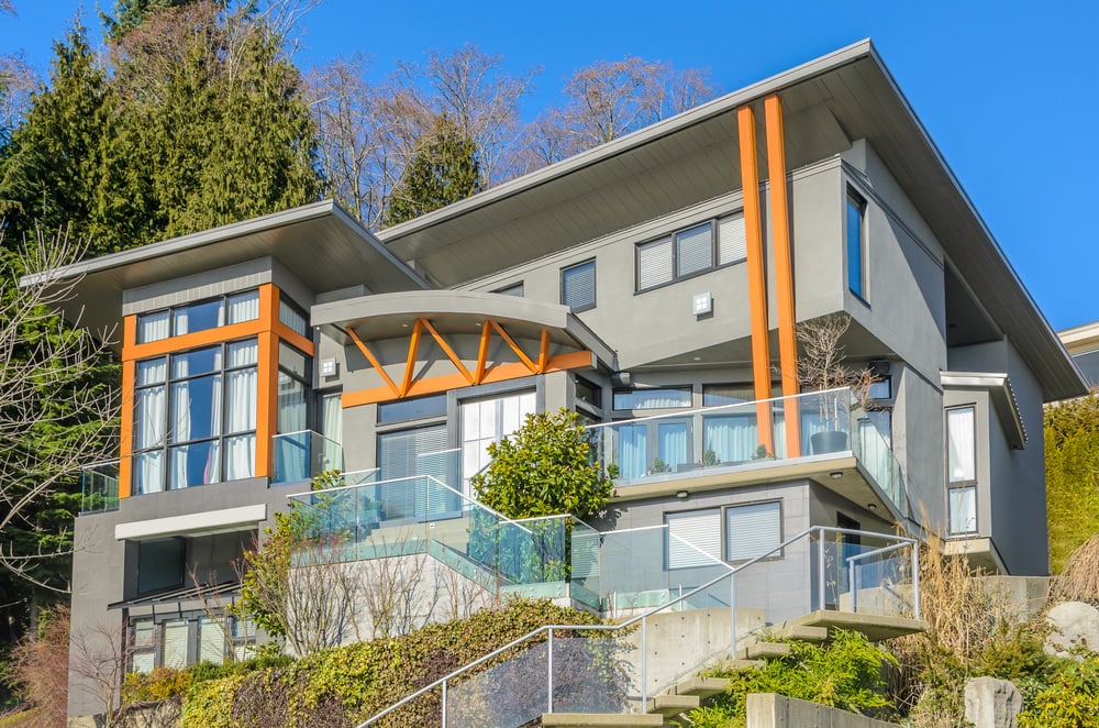 一个现代的房子，灰色的外观与木材色调的口音。它的楼梯和阳台区域都有玻璃栏杆。它还有一个后院，有一套很好的设施。