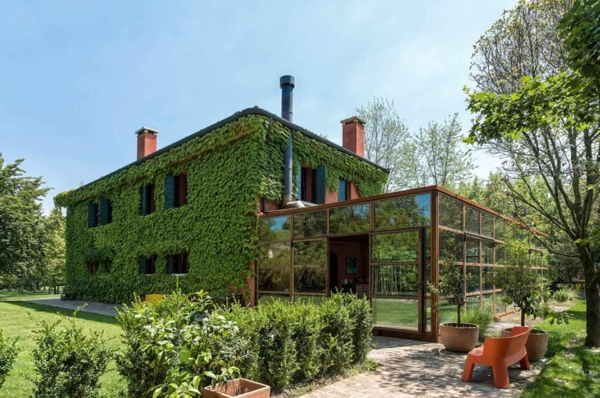 这座房子的红色外墙被绿色植物覆盖着。它还有一个宽阔的院子，有维护良好的草坪区域，植物和树木。