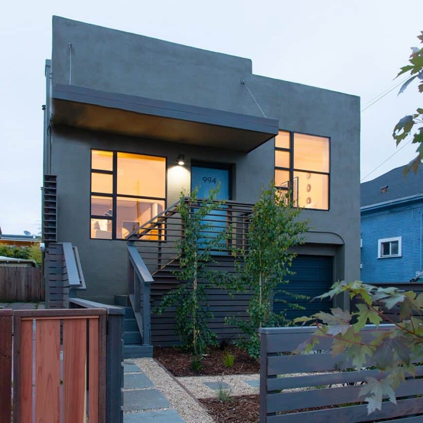 一座现代的房子，拥有时尚的灰色外墙和玻璃窗。它有一个漂亮的院子，有一条由时尚的栅栏保护的走道。