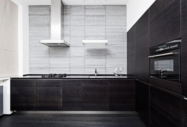 这是一个简单的双色调l型厨房，炭黑厨柜搭配黑色花岗岩台面。这与深色的硬木地板很好地搭配，并与浅灰色的墙壁和明亮的白色天花板形成对比。