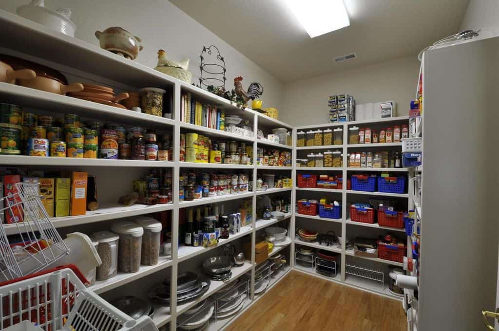 这是一个简单的步入式厨房食品储藏室，墙壁上布满了浅灰色的货架，用来储存食物。架子上还有色彩鲜艳的篮子，与顶层架子上的装饰品一起突出，成为小房间的装饰。