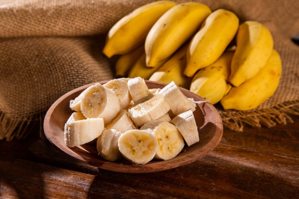 一捆成熟的香蕉和切好的香蕉放在一个木碗里。