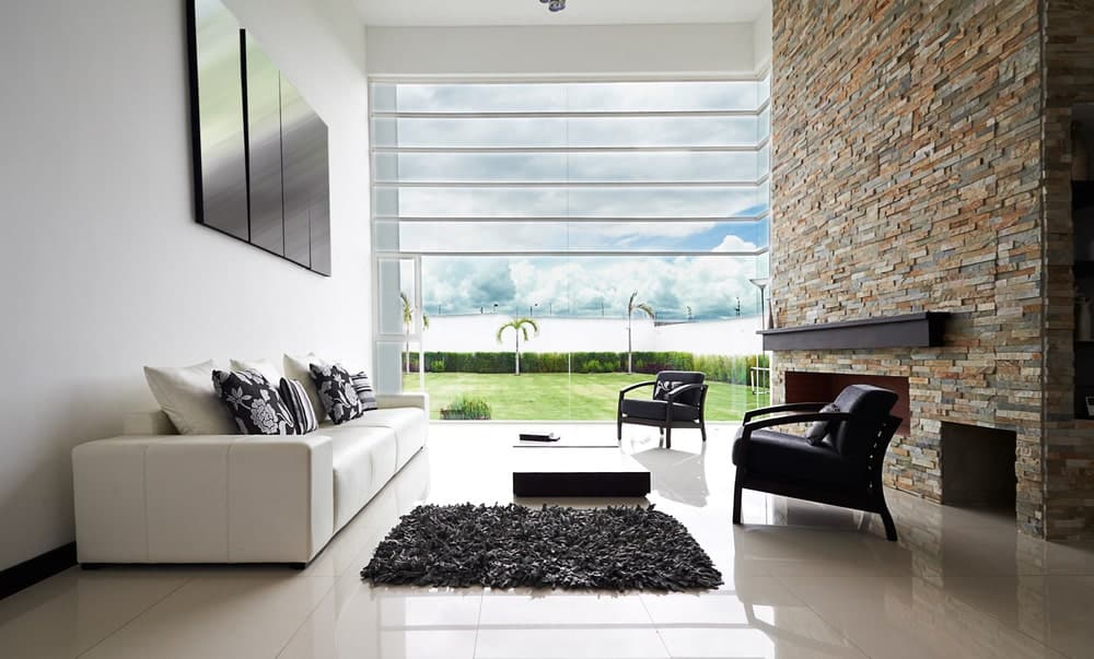 这是一间极简主义风格的客厅的全貌，有充足的自然采光、一座巨大的石头壁炉和高高的白墙。
