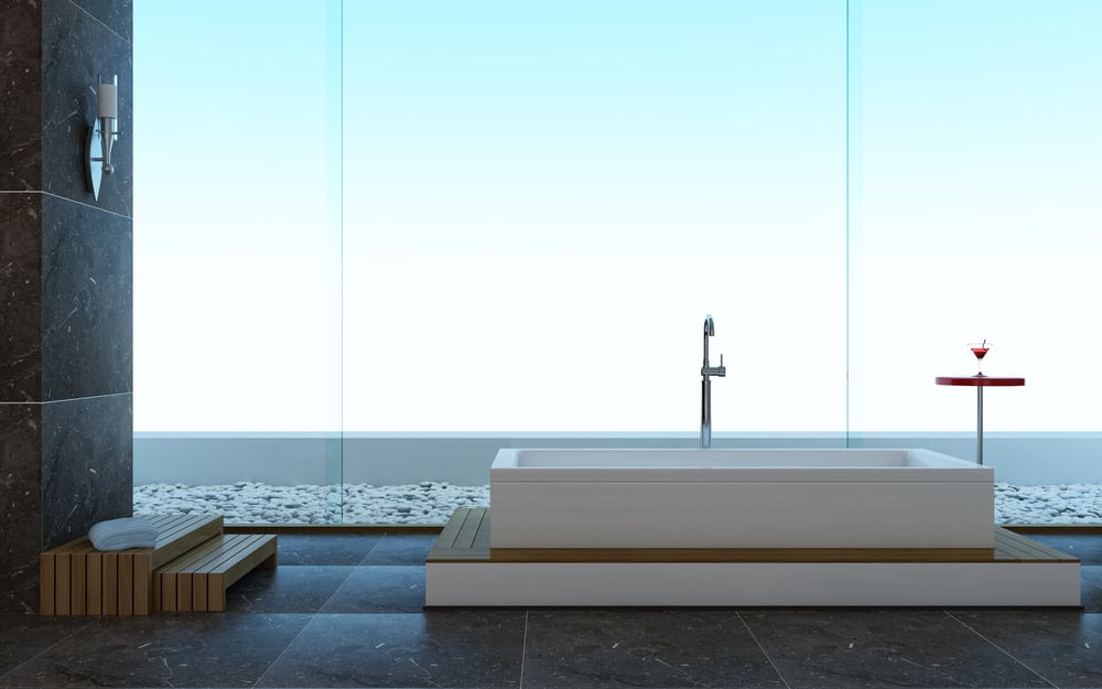 这是一间简单的主浴室，大玻璃墙旁有一个浴缸，使浴室的灰色瓷砖更加明亮。