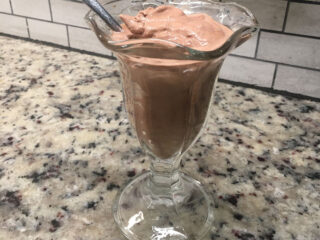 一个巧克力冰淇淋放在一个玻璃杯和一个勺子上。