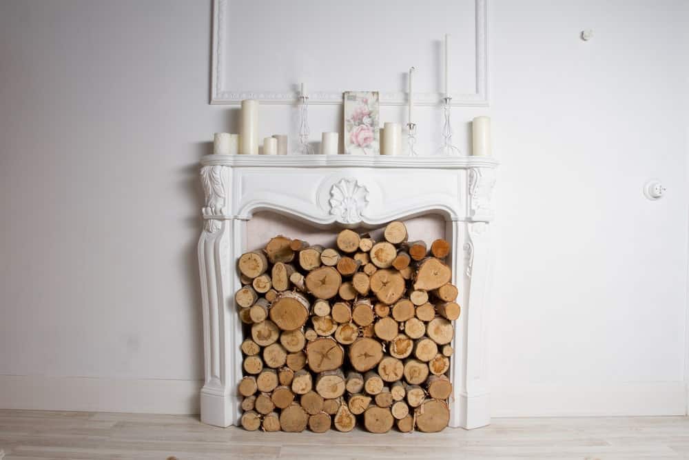 在白色壁炉上存放在边缘的木柴，在壁炉架上的不同尺寸的蜡烛。