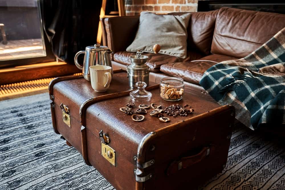 巧克力色的储存行李箱用作咖啡桌在起居室有匹配的皮革沙发和区域地毯。