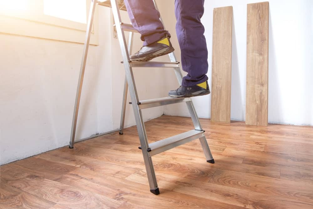 攀登或爬上一个梯子的一个人的脚的裁剪射击在有木地板的一个房间里。