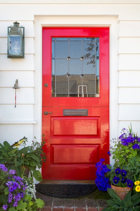 一扇真正引人注目的经典红色门。它配有迷人的青铜把手和与玻璃烛台和安装在白色壁板上的小钟相匹配的板。