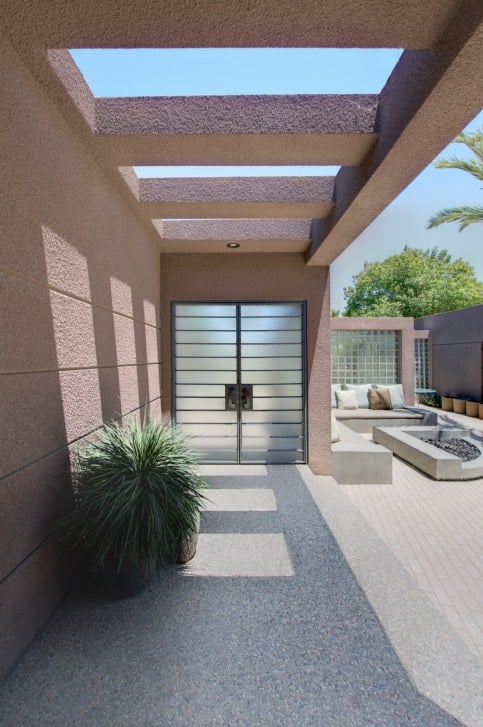带有水平窗格的磨砂玻璃双门，从混凝土梁上保持现代房子的凝聚力，继续前往米色墙壁。绿色盆栽植物在该地区增加了柔软的外观。