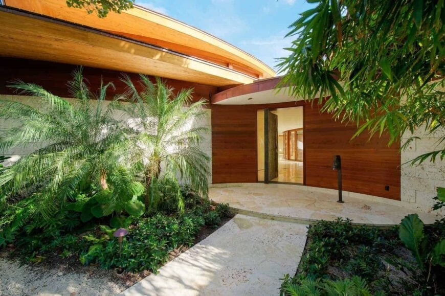 一条带有配套平台的石板走道通向黑色木质前门，以非传统的方式打开。它辅以热带植物，为房子增添了美好的感觉。