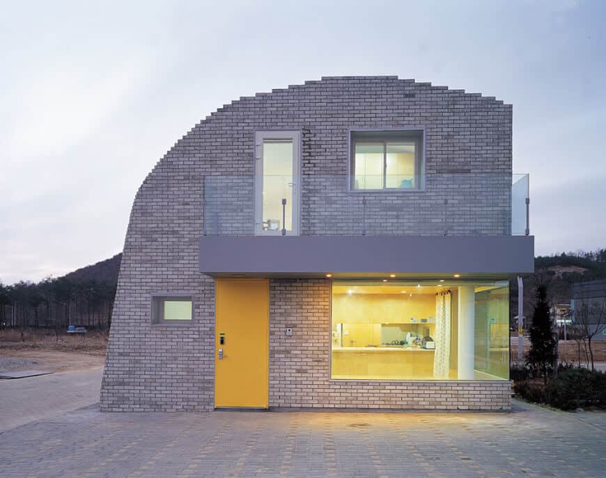 一个现代化的房子，有一个混凝土外观。提供带玻璃栏杆的阳台。房屋还有玻璃窗。