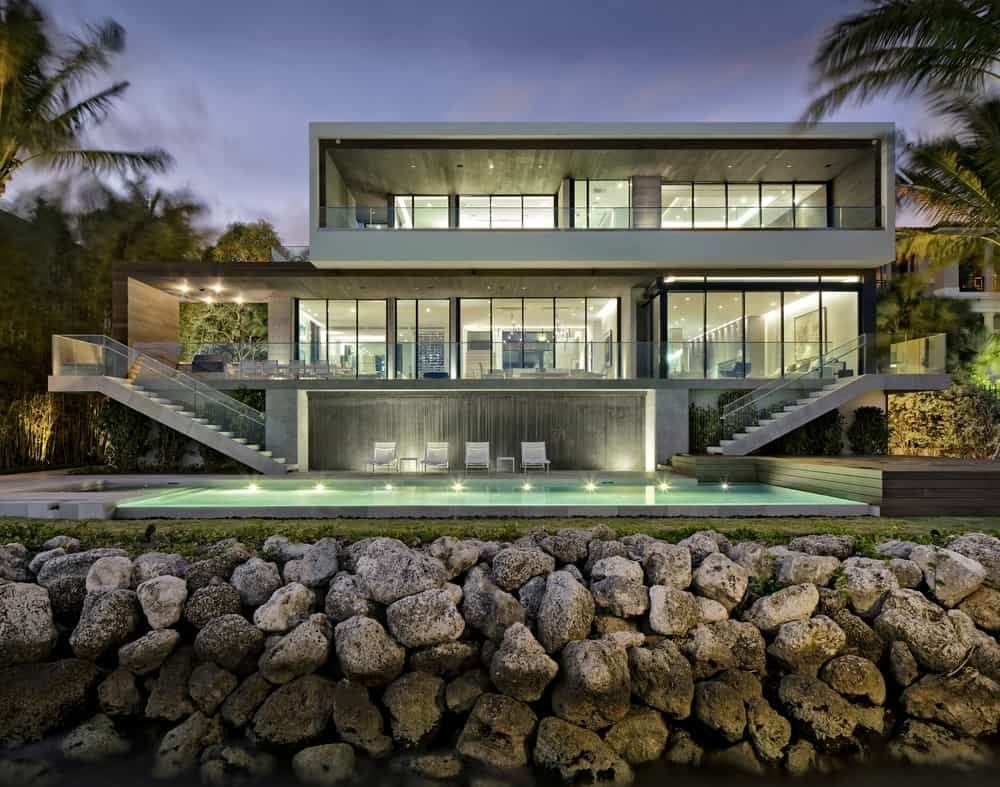 一座现代住宅拥有简约的设计，坐落在石头挡土墙的顶部。这两端都有宽敞的阳台和混凝土楼梯，通往宁静的游泳池。